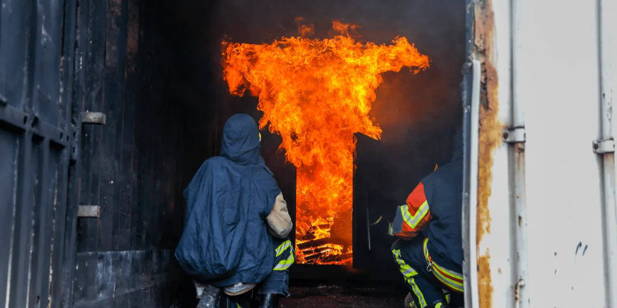 Feuerwehrleute nähern sich einer Tür mit herausschlagenden Flammen bei einem Flashover.
