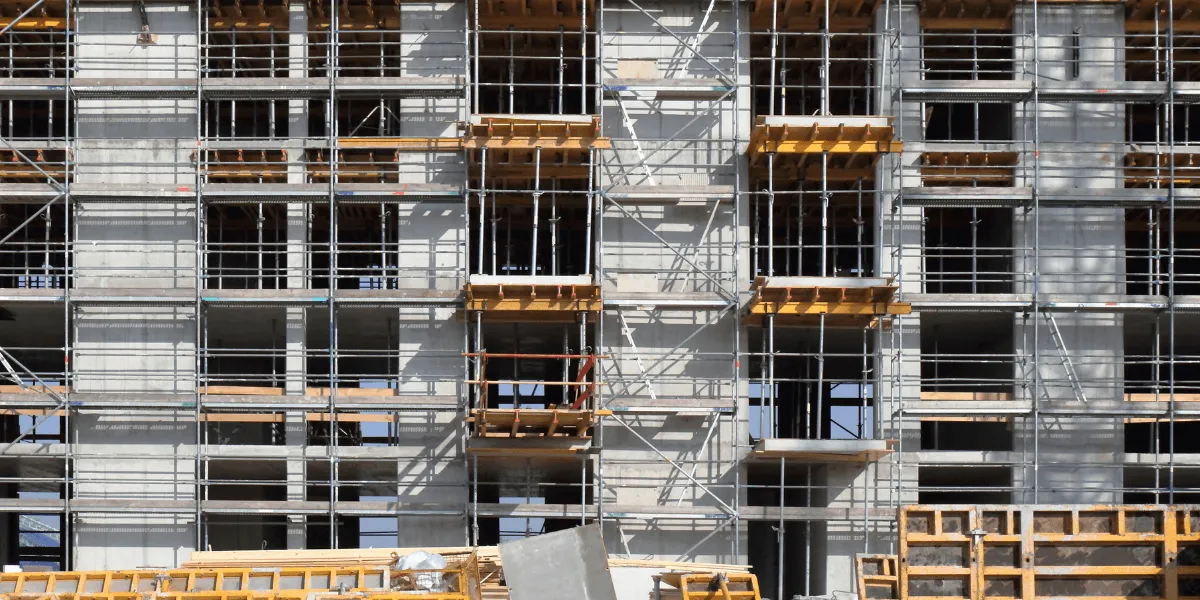 Holztafelbauweise: mehrgeschossiger Rohbau mit Gerüst, Betonwänden und Holzschalungen auf einer Baustelle.