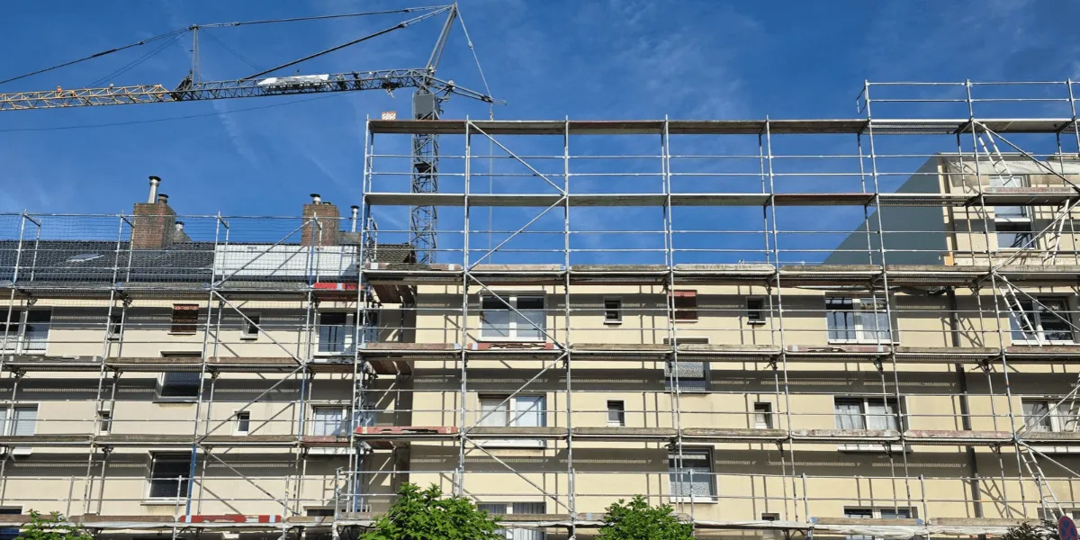 Serielle Sanierung: Baustelle mit einem mehrstöckigen Gebäude im Rohbau, umgeben von Baugerüsten und einem großen Kran vor blauem Himmel.