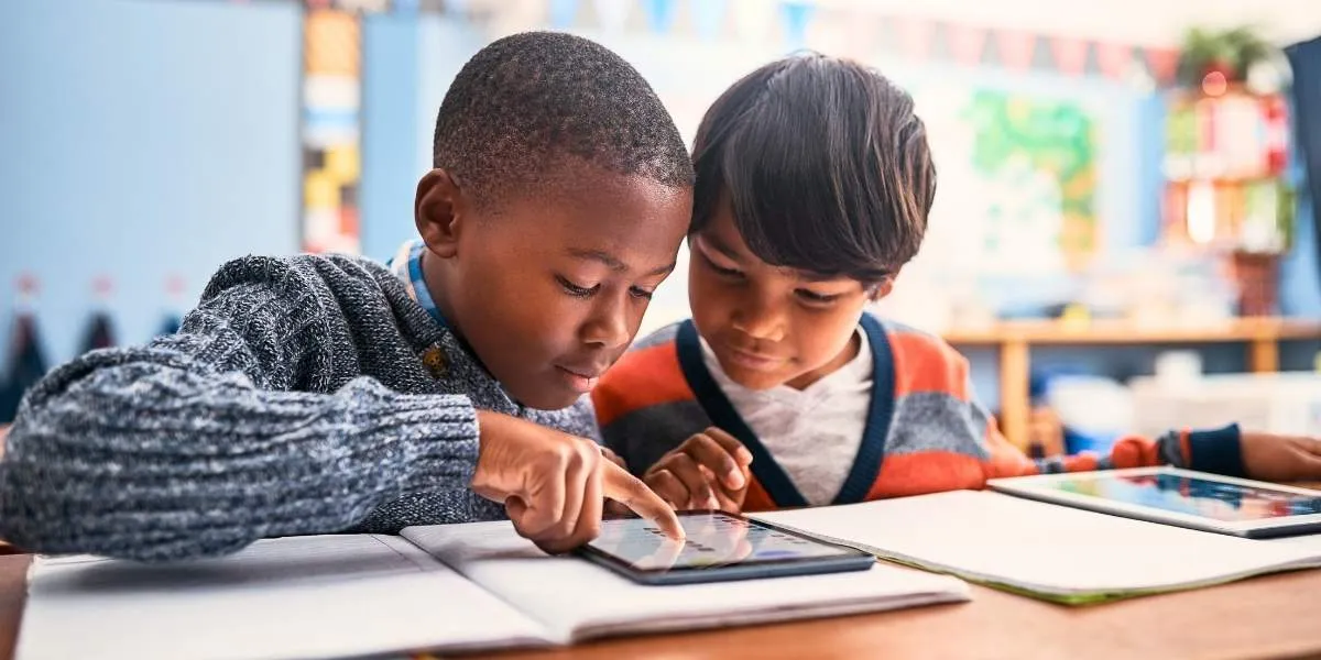 Medienkonsum Kinder: Zwei ca. 10-jährige Schüler arbeiten gemeinsam an einem Tablet in einem Klassenzimmer