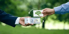 BEHG: Zwei Hände tauschen vor grünem Naturhintergrund einen Bündel US-Dollar-Banknoten gegen eine Karte mit CO2-Symbol – symbolisiert den Handel mit CO2-Zertifikaten bzw. den Emissionshandel.