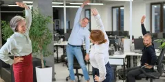 Vier Angestellte machen Dehnübungen im Büro als Teil der betrieblichen Geundheitsförderung