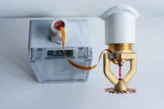 Sprinkleranlage mit transparenter Auslöseeinheit und kupferfarbener Leitung an einer weißen Decke.