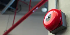 Roter manueller Brandmelder an einer Wand in einer Industriehalle mit sichtbaren Stahlträgern im Hintergrund.