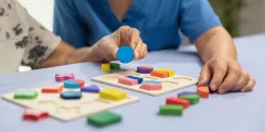 Ältere Frau und Pflegekraft spielen gemeinsam ein hölzernes Formpuzzle zur Demenzvorbeugung