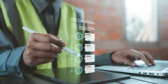 DIN EN ISO 9001: eine Person in Warnweste bedient mit einem Stift ein Tablet; darüber ist eine digitale Oberfläche mit dem Text „ISO Compliance“ und Symbolen für Prüf- und Zertifizierungsprozesse eingeblendet.