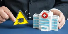 KHAG: Geschäftsmann hält ein Modell eines Krankenhauses neben ein gelbes Warnschild mit Doktorhut als Symbol für Risiken oder Herausforderungen im Gesundheits- und Bildungsbereich.