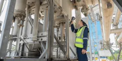 KRITIS-Dachgesetz: Mitarbeiter in Schutzhelm und Warnweste prüft Industrieanlagen mit einer Taschenlampe.