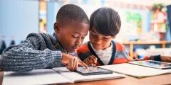 Medienkonsum Kinder: Zwei ca. 10-jährige Schüler arbeiten gemeinsam an einem Tablet in einem Klassenzimmer
