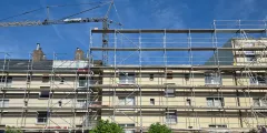 Serielle Sanierung: Baustelle mit einem mehrstöckigen Gebäude im Rohbau, umgeben von Baugerüsten und einem großen Kran vor blauem Himmel.