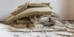 TRGS 521: Stapel alter, beschädigter Mineralwolle-Dämmplatten (Steinwolle) mit bröckelnden Kanten und Staub, liegend auf einem mit Farbresten bedeckten Boden – vermutlich im Rahmen eines Rückbaus oder einer Sanierungsarbeit fotografiert.